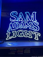 Close-up photo of the neon sign showing the blue 'SAM ADAMS' and white 'LIGHT' illuminated text.