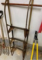 Metal sled frame with rust and signs of use, photographed standing with gardening tools in background.