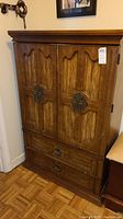 Front view of the vintage Bassett armoire showing two paneled doors with ornate metal handles and two drawers below, medium brown wood finish.