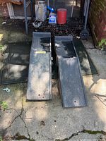Photo of two black plastic car ramps placed side by side on a concrete surface outdoors.