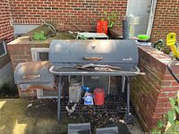 Full side view of the Char-Broil grill with attached smoker chamber showing rust, general wear, and tools stored on lower rack.