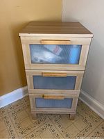 Frontal view of wooden chest with three drawers showing the frosted ribbed glass fronts and wooden handles