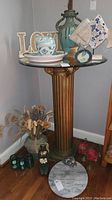 Full view of gold decorative column table with items on glass top and various decorative objects at base.