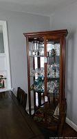 Front angled view of the dark wood display cabinet showing glass shelves, mirrored back and sides, wooden framed glass door, and decorative molding.