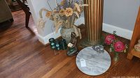 Lot showing large vase with beige faux flowers, bronze sculpture vase, tealight candle votives, round marble tray with silver decorative object, and two pink flowering stems in glass vases on wooden floor.