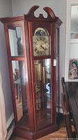 Full view of the tall dark wooden grandfather clock showing glass front and side panels and the missing door handle area at top.