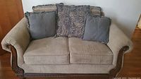 Front view of olive green loveseat sofa showing rolled arms with wood trim and five accent cushions in patterned and solid fabrics.