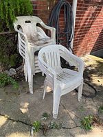 Nine white weathered PVC patio chairs stacked outside on concrete, showing dirt and signs of outdoor wear.