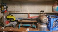 Ryobi circular saw with yellow and black painting, vintage heater, several hand tools and containers on wooden shelves, some rust visible.