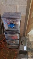 Plastic storage drawers and bins containing assorted hand tools including pliers and sockets, and metal toolbox with handle.