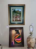 Two framed embroidered wall art pieces displayed side by side on a wall, one depicting a garden scene and the other two women in traditional dress.