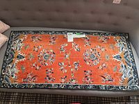 Full view of orange-red embroidered runner laid flat on sofa