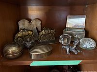 Full view of the shelf containing the collection of metal and crystal items including trinket boxes, bookends, paperweights, and figurines.