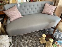 Front angled view of grey tufted sofa with two pink cushions