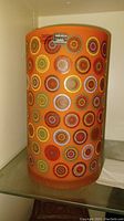 Front view of orange cylindrical vase with multicolor concentric circle motifs