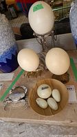 Three faux ostrich eggs on three different metal stands, small bowl of marble eggs and silver-tone crab figurine arranged on table
