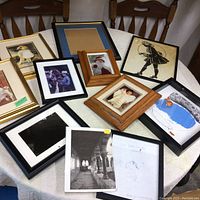 Overview photo of multiple framed artworks arranged on table, shows various sizes and frame styles.
