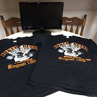 Two black Biker Beer t-shirts and an LG monitor displayed on a table with chairs.