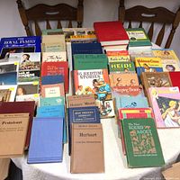 Shows a tabletop view of approximately 38 vintage hardcover and paperback books arranged closely together. Titles visible include Sleeping Beauty, Trixie Belden, The Royal Family, The Tale of Peter Rabbit, Heidi, Robinson Crusoe, Pestalozzi, and others. Books vary in color and condition.