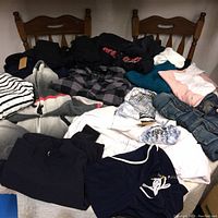 Overview of various folded clothing items on a table including sweatshirts, denim jacket, Under Armour shirt, sweatpants, and casual tops.