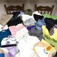 Photo showing a variety of folded clothing including shorts, shirts, and vests layered on chairs