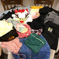 Photo showing a variety of women's clothing including jeans, a Christmas-themed sweater with reindeer, shorts, shirts, and hats in different colors and patterns.