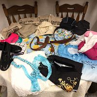 Overall view of all clothing and accessories displayed on table and chairs showing variety of shirts, caps, belts, tote bags, and shoes.