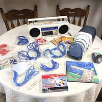 Wide shot of Sony cassette player radio, multiple Ethernet cables, digital photography book, computer mouse, CD cases, and other accessories on round table.