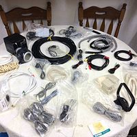 Table setup showing multiple electronic cables, USB cords, AV RCA cables, Rockband USB port, water clock, and wires sea in plastic bags and coiled on table surface.