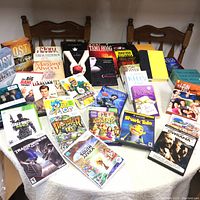 Photo showing a large variety of DVDs, Nintendo Wii video games, and paperback books arranged on a table and chairs