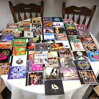 Wide view of multiple CDs spread out on a table showing various artists and compilation albums.