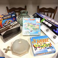 Photo showing collection of boxed Angry Birds Star Wars game, Audio Bingo game, Scrabble Junior game, bathroom light fixture parts including frosted glass cover and black base, metal cross item, and black CD case box.