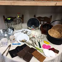 Overview of multiple household items including wallets, cutlery, mugs, baskets, blender container, and kitchen tools shown on a table and chairs