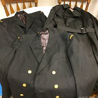 Three black jackets laid on chair showing two Canadian Armed Forces jackets with gold buttons and Canada patches, and one black Moores trench coat with belt.