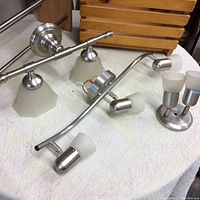 Photo showing three retro light fixtures with brushed metal bases and frosted glass shades, with wooden shoe and magazine racks in the background.