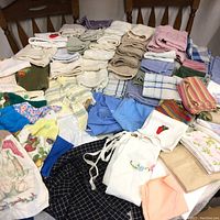 Wide view of assorted folded linen textiles arranged on a chair including hand towels, face cloths, dish towels, and bath towels in various colors and patterns.