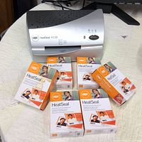 GBC HeatSeal H110 laminator with multiple boxes of HeatSeal laminating pouches on a white cloth surface.