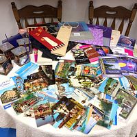Table with vintage postcards spread out showing various buildings, scenic views, and landmarks alongside Crown Royal glasses, gift bags, and books.