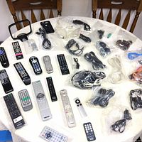 Overview of remote controls spread out on a table alongside multiple cables and accessories in plastic bags