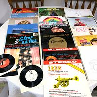Top view of 15 vinyl record covers and 2 single vinyl 45 RPM records spread on table, showing artists including Kenny Rogers, Glenn Miller, Bob Newhart, Anne Murray, and others.