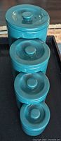 Four green ceramic canisters stacked nesting with lids on top, glossy finish visible