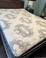 Photo of queen size mattress top showing white fabric with grey ornamental patterns and tufting buttons