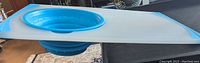 Rubbermaid combined cutting board and turquoise silicone collapsible colander placed on a surface