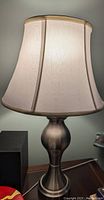 Photo showing beige fabric lamp shade in a bell shape with vertical seams.