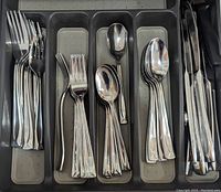 Silver stainless steel forks, knives, and spoons arranged in a tray.