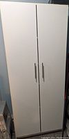 Closed front view of white cabinet with two vertical doors and silver handles.