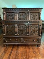 Front image of wooden bed frame showing three carved panels with floral and geometric designs and two drawers with wooden knobs at the footboard.