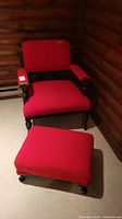 Wood framed vintage chair with red upholstery including carved wood details on the arms and legs, photographed from the front in a corner