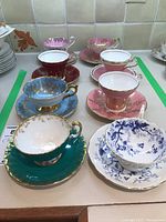 Overview image showing eight bone china tea cups and matching saucers in various colors and patterns arranged on a countertop.
