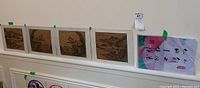 Five mounted artworks aligned on a ledge including four landscape drawings and one calligraphy piece.